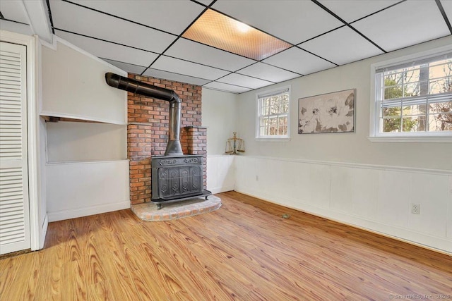 unfurnished living room with a wood stove, a healthy amount of sunlight, light wood-style floors, and a wainscoted wall