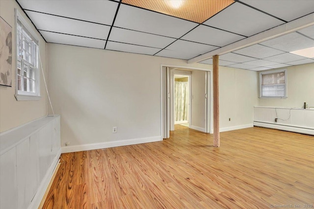 basement featuring light wood-type flooring, a paneled ceiling, baseboards, and a baseboard radiator