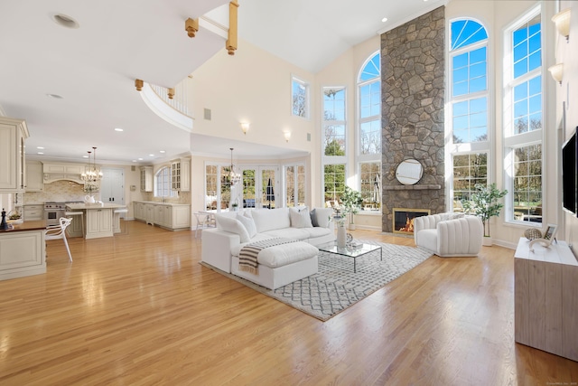 living room with a towering ceiling, a stone fireplace, a chandelier, and light hardwood / wood-style flooring