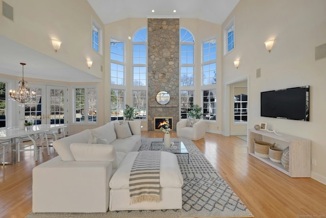 living room featuring a stone fireplace, high vaulted ceiling, an inviting chandelier, and light hardwood / wood-style flooring