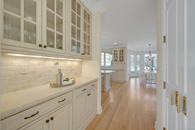 bar with tasteful backsplash, light stone counters, decorative light fixtures, light hardwood / wood-style flooring, and ornamental molding