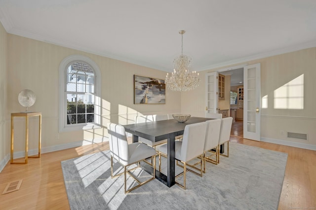 dining space featuring a notable chandelier, crown molding, light hardwood / wood-style floors, and french doors