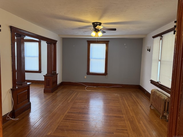 spare room with radiator heating unit, decorative columns, dark hardwood / wood-style flooring, ceiling fan, and a textured ceiling