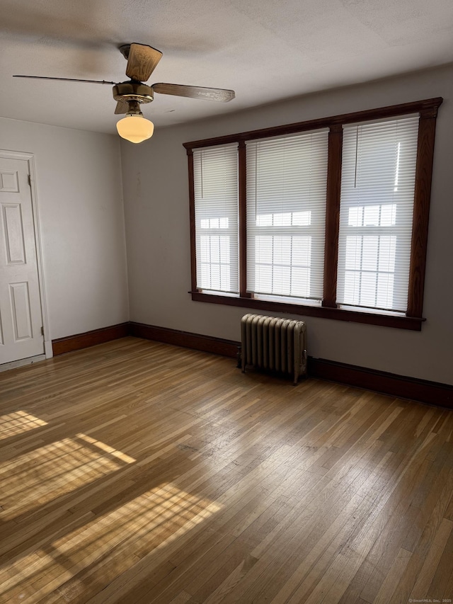 empty room featuring ceiling fan, a healthy amount of sunlight, radiator, and hardwood / wood-style floors