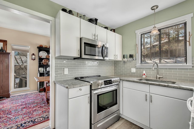 kitchen featuring sink, appliances with stainless steel finishes, white cabinetry, backsplash, and hanging light fixtures