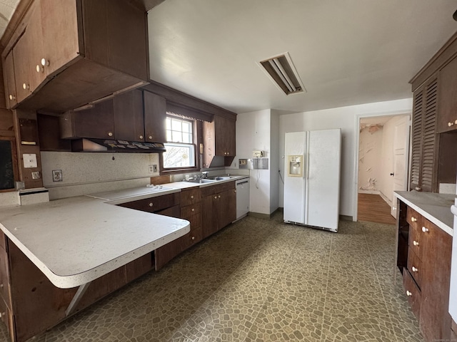 kitchen with white appliances, a breakfast bar area, a peninsula, light countertops, and a sink