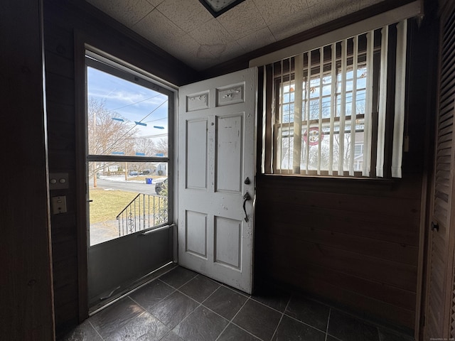 entryway with wood walls, plenty of natural light, and dark tile patterned floors