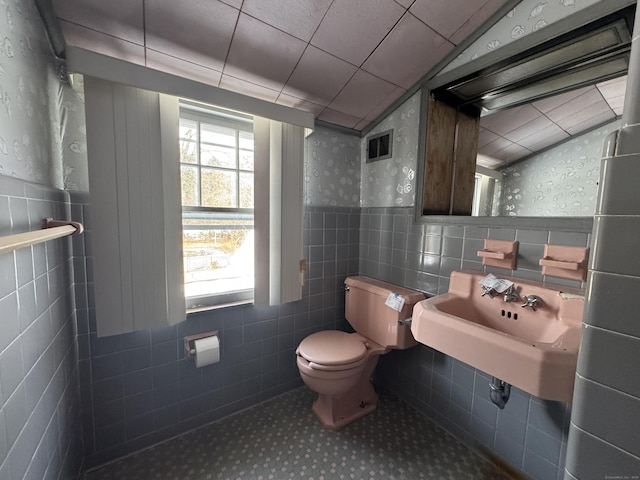 bathroom with a wainscoted wall, tile walls, lofted ceiling, visible vents, and toilet