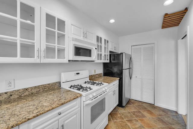 kitchen with light stone countertops, white cabinets, and white appliances