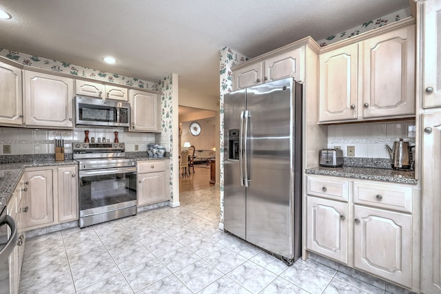 kitchen featuring tasteful backsplash, stainless steel appliances, a textured ceiling, dark stone counters, and light tile patterned floors