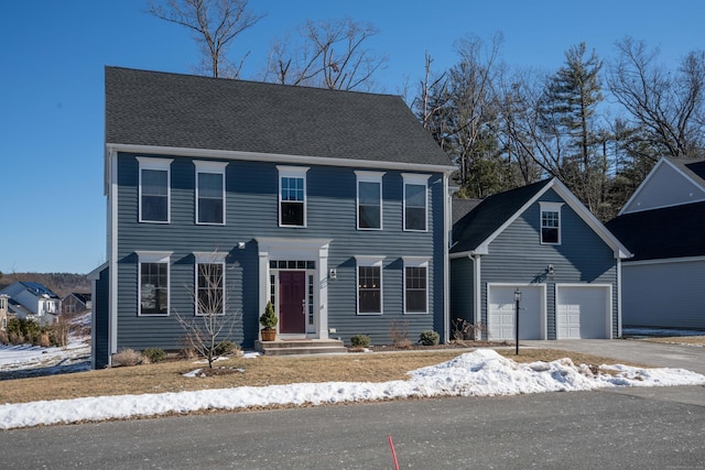 colonial inspired home with aphalt driveway, roof with shingles, and a garage