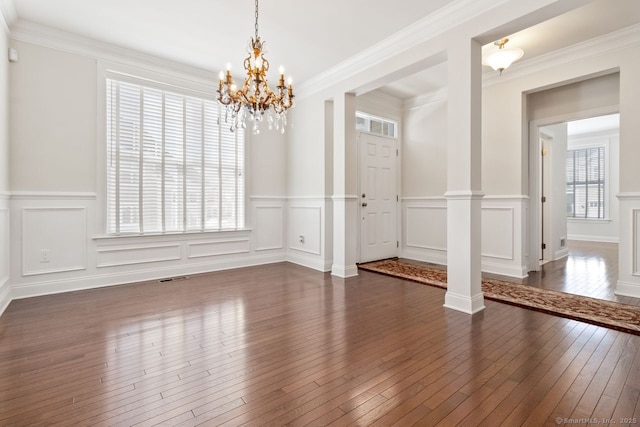 unfurnished room featuring dark wood-type flooring, crown molding, an inviting chandelier, and ornate columns