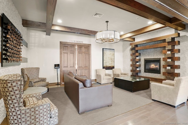 living room featuring an inviting chandelier, beam ceiling, light hardwood / wood-style floors, and a large fireplace