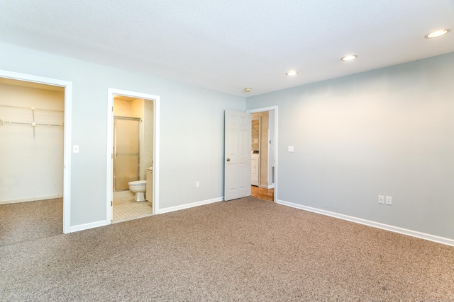 unfurnished bedroom with a closet, connected bathroom, a spacious closet, and carpet