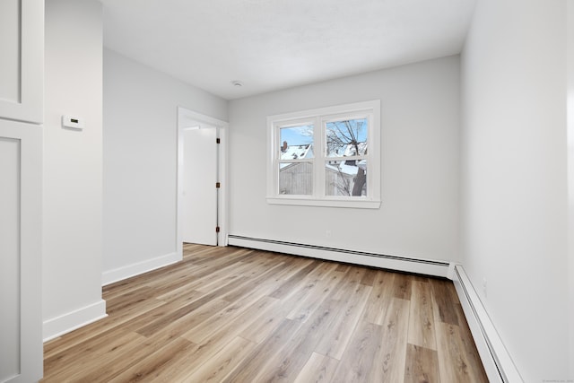 spare room featuring baseboard heating and light hardwood / wood-style floors