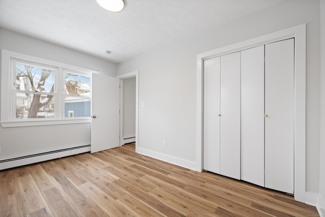 unfurnished bedroom featuring a baseboard heating unit and light hardwood / wood-style floors