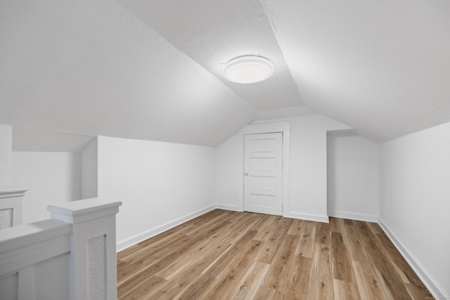 additional living space featuring lofted ceiling, light hardwood / wood-style floors, and a textured ceiling