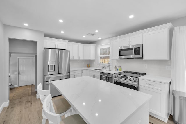 kitchen with stainless steel appliances, white cabinetry, a center island, and sink