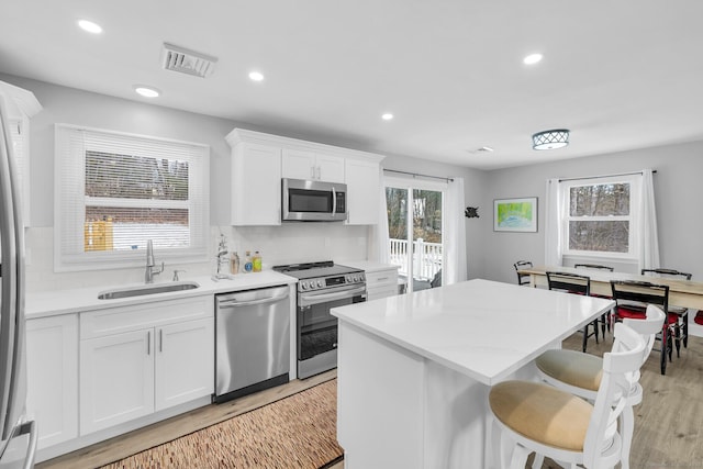 kitchen with a kitchen island, sink, white cabinets, stainless steel appliances, and light hardwood / wood-style flooring