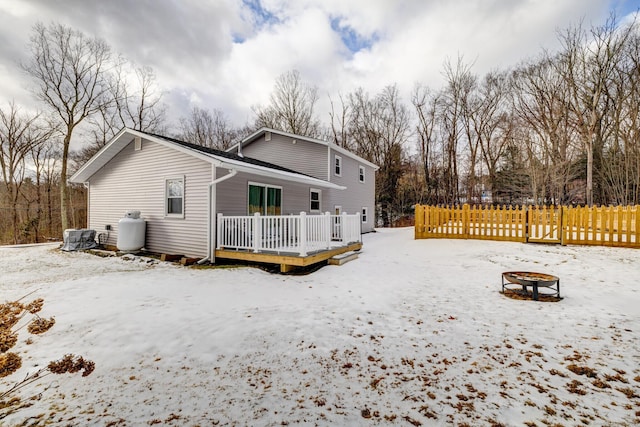 snow covered rear of property with a wooden deck, central AC unit, and an outdoor fire pit