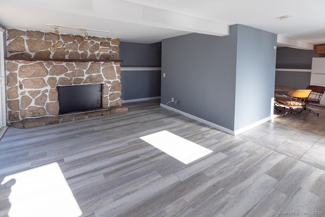 unfurnished living room with wood-type flooring, a stone fireplace, and beam ceiling