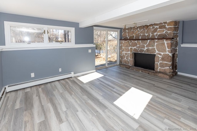 unfurnished living room with light hardwood / wood-style flooring, a baseboard heating unit, beam ceiling, a fireplace, and track lighting