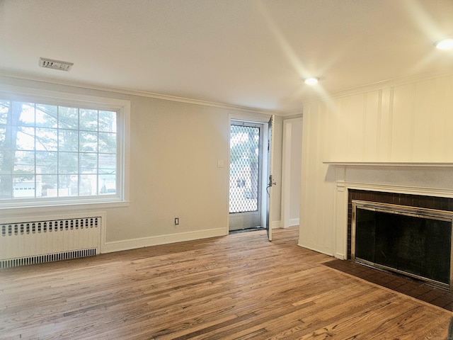 unfurnished living room with crown molding, radiator heating unit, hardwood / wood-style floors, and a tile fireplace