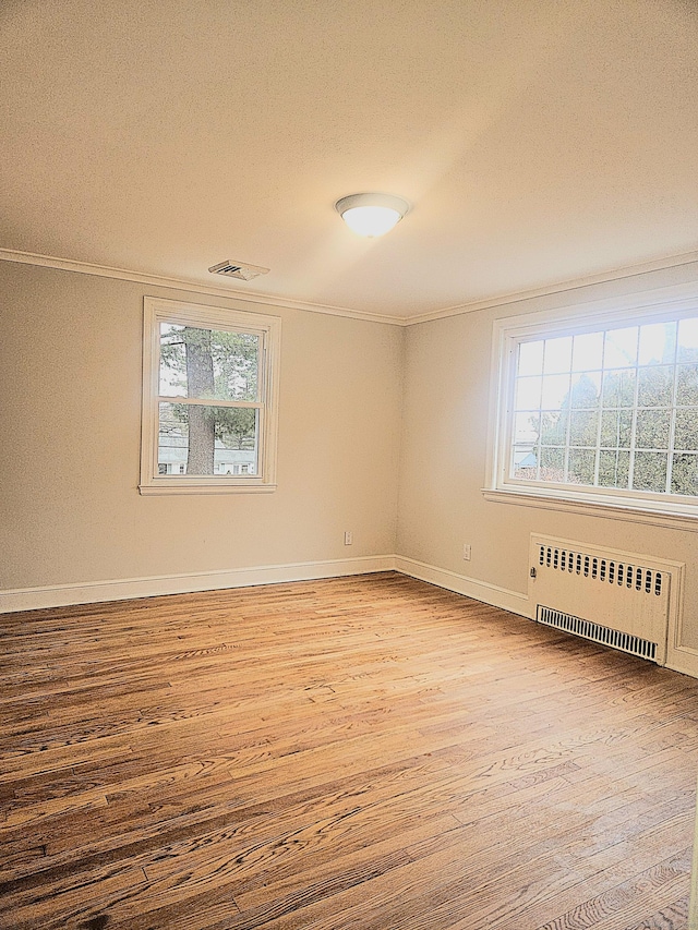 empty room with ornamental molding, radiator, light hardwood / wood-style flooring, and a wealth of natural light