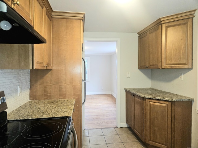 kitchen with electric stove, light tile patterned floors, tasteful backsplash, ornamental molding, and light stone countertops