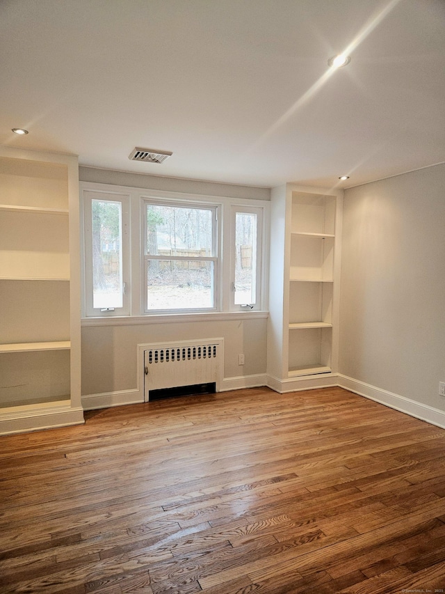 spare room with radiator heating unit, built in features, and wood-type flooring