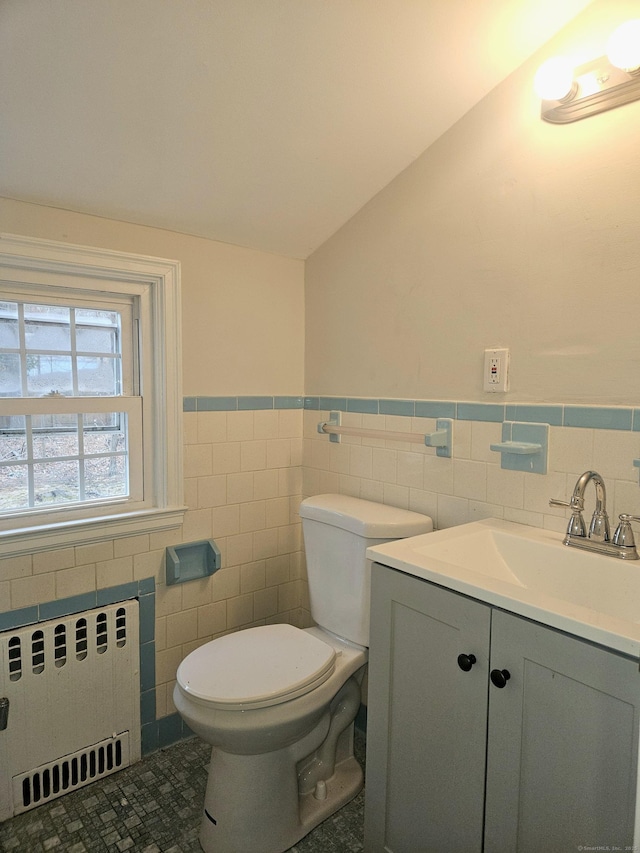 bathroom featuring vaulted ceiling, radiator, tile walls, vanity, and toilet