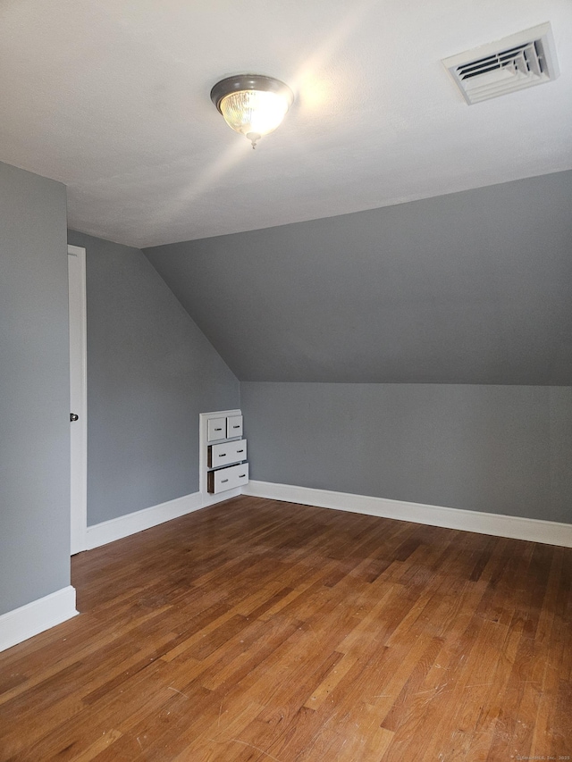 additional living space with hardwood / wood-style floors and vaulted ceiling