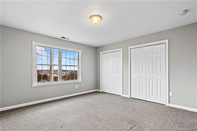 unfurnished bedroom featuring carpet flooring and two closets