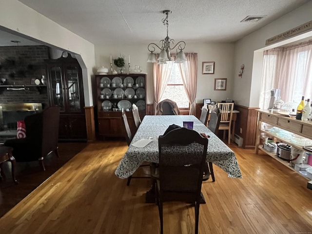 dining room with a baseboard radiator, hardwood / wood-style floors, a textured ceiling, and an inviting chandelier