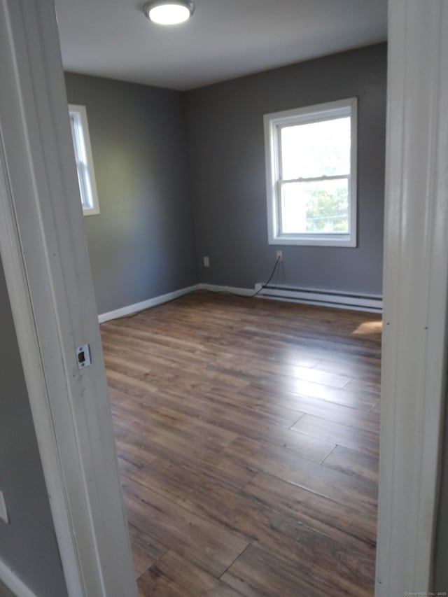 empty room with dark hardwood / wood-style flooring and a baseboard heating unit