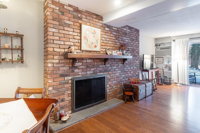 living room featuring a fireplace, hardwood / wood-style floors, and a wall unit AC