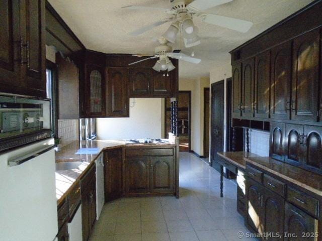 kitchen with ceiling fan, black microwave, dark brown cabinetry, white dishwasher, and tile countertops