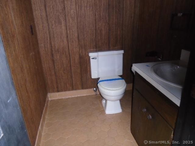 bathroom with tile patterned flooring, vanity, wooden walls, and toilet