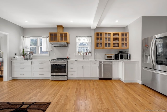 kitchen with sink, white cabinetry, beam ceiling, stainless steel appliances, and light wood-type flooring