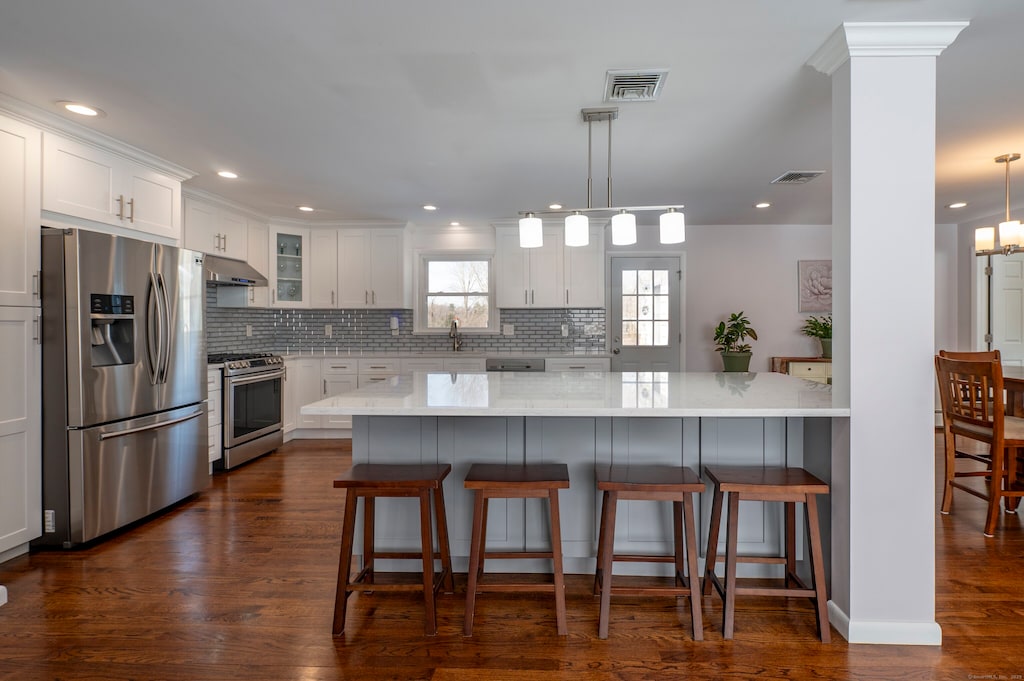 kitchen featuring decorative light fixtures, tasteful backsplash, white cabinetry, stainless steel appliances, and light stone countertops