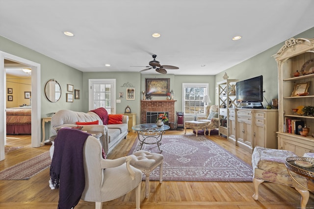 living room with ceiling fan, light hardwood / wood-style floors, and a brick fireplace