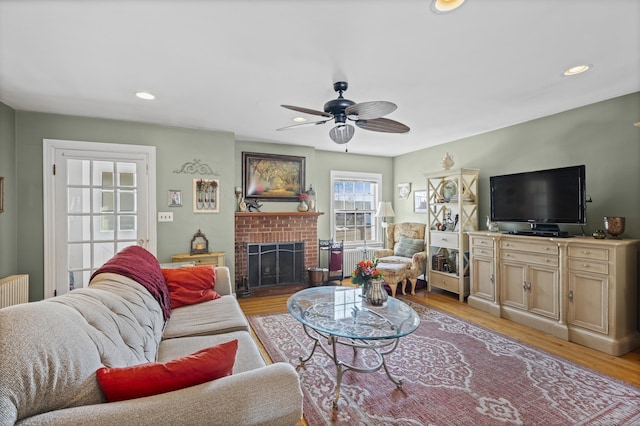 living room featuring a brick fireplace, ceiling fan, and light wood-type flooring