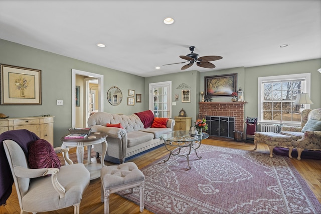 living room featuring a brick fireplace, hardwood / wood-style flooring, radiator, and ceiling fan