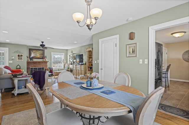 dining room with a brick fireplace, ceiling fan with notable chandelier, and light hardwood / wood-style floors