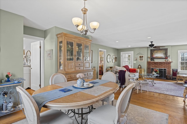 dining area featuring a fireplace, ceiling fan with notable chandelier, and light wood-type flooring