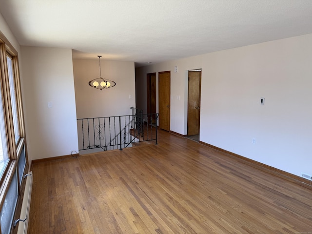 empty room featuring visible vents, baseboards, light wood finished floors, and a baseboard radiator