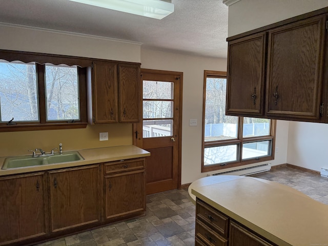 kitchen with a sink, light countertops, stone finish floor, a textured ceiling, and baseboard heating