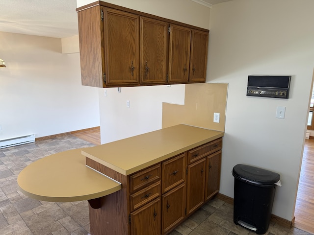 kitchen with brown cabinetry, baseboards, a peninsula, light countertops, and stone finish floor