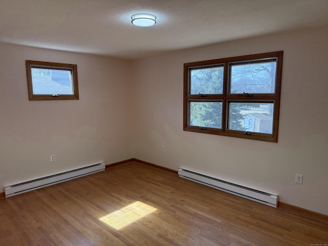 unfurnished room featuring a baseboard heating unit, light wood-style floors, baseboards, and baseboard heating