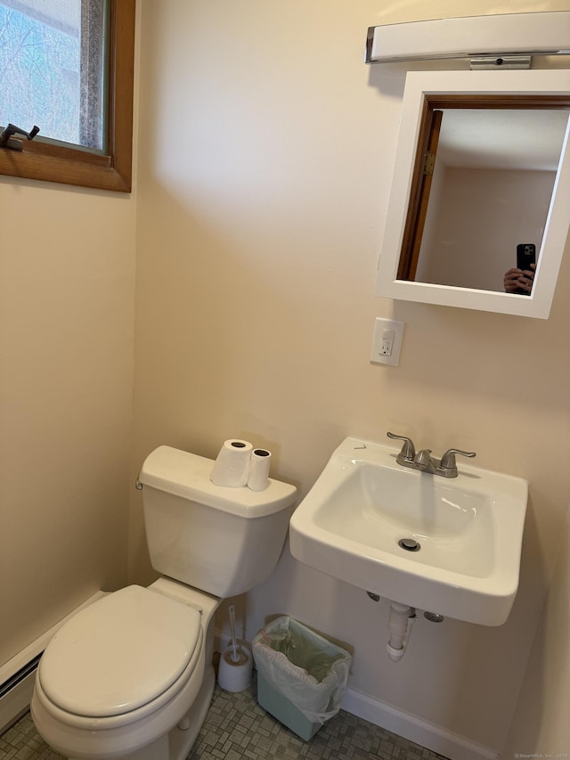 half bathroom with toilet, a baseboard heating unit, and a sink